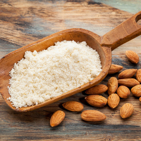 Wooden scoop filled with almond flour on a wooden surface with organic almonds around