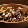 Wooden bowl filled with organic muesli, dried fruits, and nuts with a wooden spoon.
