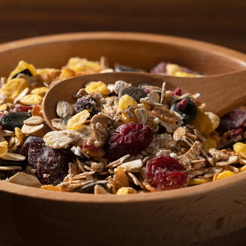 Wooden bowl filled with organic muesli, dried fruits, and nuts with a wooden spoon.