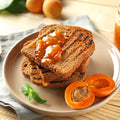 Toast with organic apricot jam on a plate with fresh apricots and mint leaves.