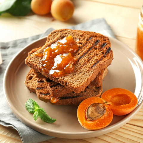 Toast with organic apricot jam on a plate with fresh apricots and mint leaves.