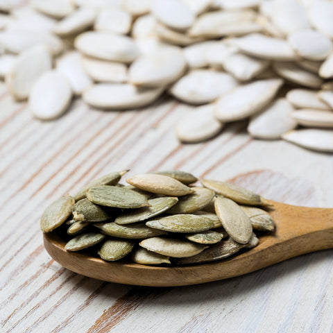 Wooden spoon filled with organic Austrian pumpkin seeds on a wooden surface with more seeds in the background.