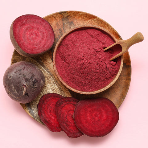 Organic beetroot powder in a wooden bowl with fresh beetroot on a pink background