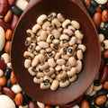 Wooden bowl filled with organic black-eyed peas surrounded by a variety of organic beans.