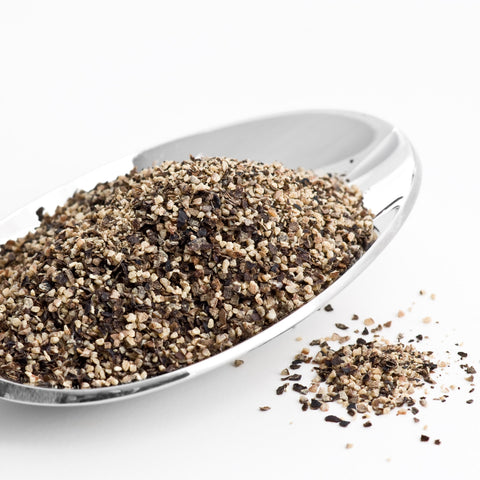White spoon filled with organic ground black pepper on a white background
