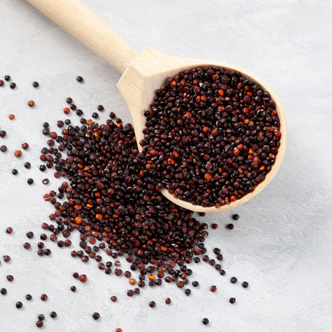 Wooden spoon filled with black quinoa seeds on a white table