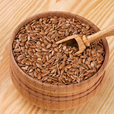 Wooden bowl filled with organic brown flax seeds on a wooden surface