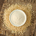 Bowl of organic brown rice flour surrounded by organic raw brown rice on a rustic background
