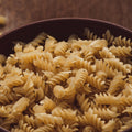 Close-up of uncooked organic brown rice flour spiral pasta in a bowl on a wooden surface
