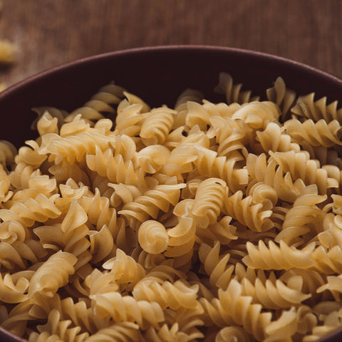 Close-up of uncooked organic brown rice flour spiral pasta in a bowl on a wooden surface