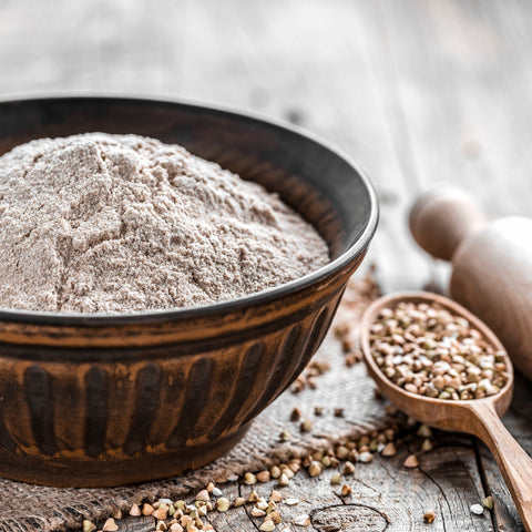 Bowl of organic buckwheat flour with buckwheat groats on a wooden surface