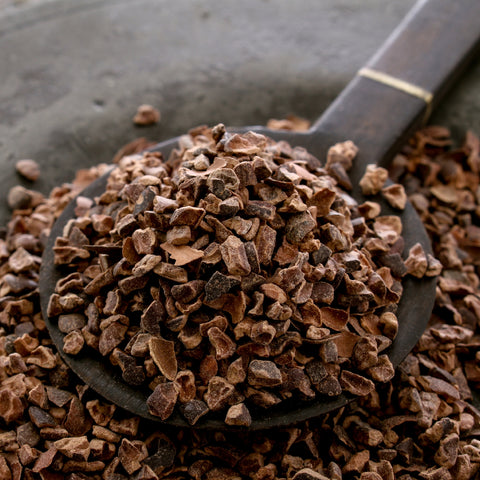 Organic cacao nibs in a wooden spoon on a dark surface