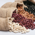 Three types of organic beans spilling out of burlap sacks on a light background