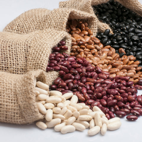 Three types of organic beans spilling out of burlap sacks on a light background