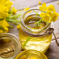 Glass jars filled with a organic canola oil, with yellow flowers on a wooden surface.