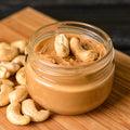 Jar of cashew butter with cashews on a wooden surface
