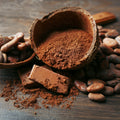 Organic cocoa powder in a shell surrounded by chocolate pieces and beans on a wooden surface