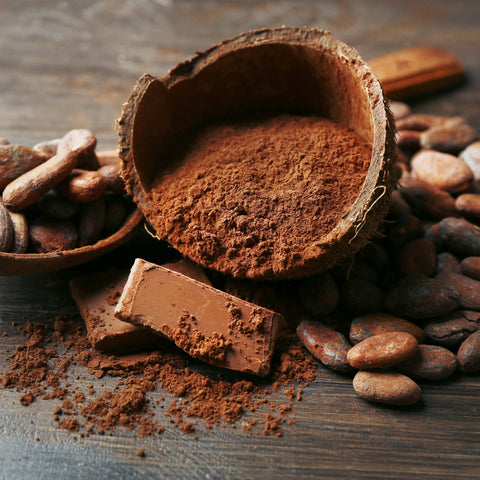 Organic cocoa powder in a shell surrounded by chocolate pieces and beans on a wooden surface