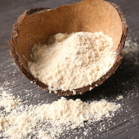 Coconut shell filled with organic coconut flour on a dark wooden surface