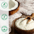 Organic coconut flour in a wooden bowl with a wooden scoop, surrounded by coconut halves, on a light background.