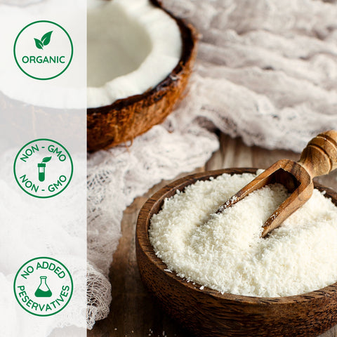 Organic coconut flour in a wooden bowl with a wooden scoop, surrounded by coconut halves, on a light background.