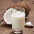 Glass of organic coconut milk with a whole and half coconut on a wooden background